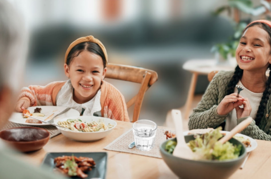 Dos niñas comiendo en la mesa con la familia.